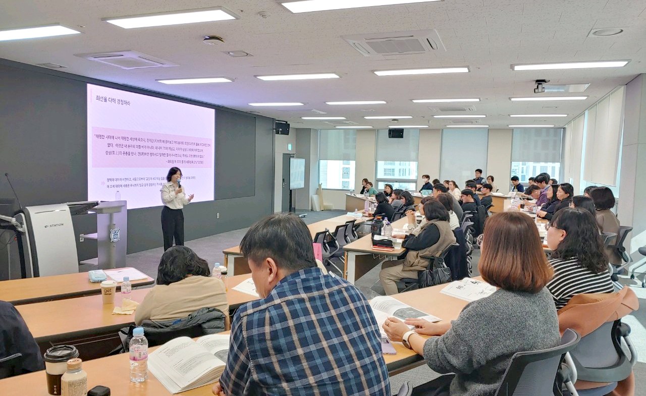 컨퍼런스룸에서 필기하며 강의를 듣는 청중